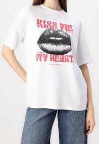 T-shirt bianco in cotone con un audace design grafico di labbra con testo rosso: "BACIAMI DOLCEMENTE" e "NON FARMi MALE". Maniche corte.
