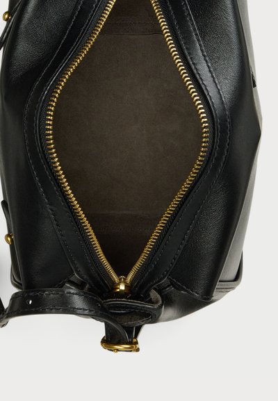 Interior de uma bolsa de couro preto com uma textura suave, apresentando um zíper dourado e um forro escuro. Destacada com uma alça e detalhes em metal.
