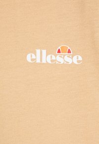 Breskovo obarvan bombažni majica z gladko teksturo, ki na sprednji strani nosi belo "ellesse" logotip ter majhen rdeč in oranžen polkrog nad njim.