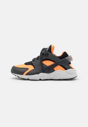 Czarno-pomarańczowy sportowy sneaker o plecionej fakturze, czarnych sznurowadłach, szarej nakrapianej podeszwie i czarnym pasku na pięcie na białym tle.
