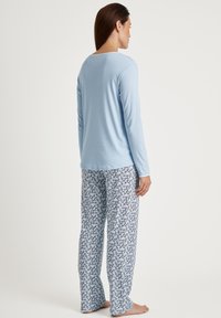 Lichtblauw langemouwen top gecombineerd met witte pyjamabroek met een blauw bloemenpatroon. Zachte, relaxte pasvorm met rechte pijpen.