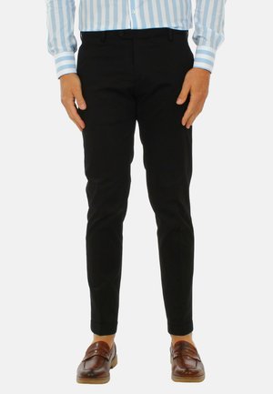 Pantaloni neri con una vestibilità slim, caratterizzati da una superficie di tessuto liscia e un orlo cropped, abbinati a mocassini marroni.