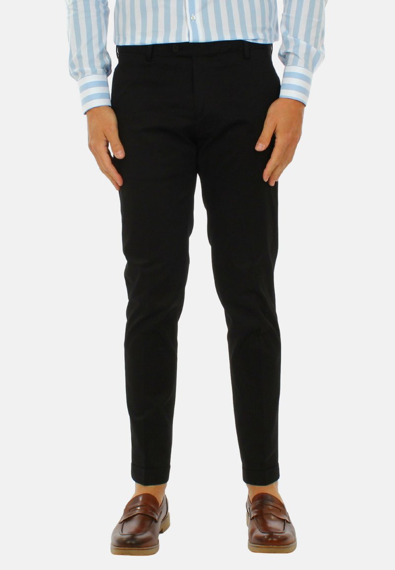 Pantaloni neri con una vestibilità slim, caratterizzati da una superficie di tessuto liscia e un orlo cropped, abbinati a mocassini marroni.