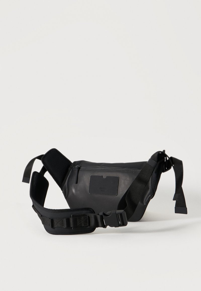 Sac banane en cuir noir avec sangle rembourrée et ajustable, poche avant zippée, et petit détail de patch rectangulaire sur le devant.