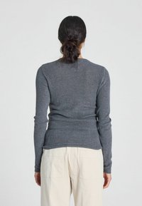 Pulover gri ajustat cu mâneci lungi și textură ribbată. Dispune de un decolteu rotund și este combinat cu pantaloni de culoare deschisă.