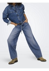 Chemise en denim oversize avec fermeture à boutons et poche poitrine, associée à un pantalon en denim à jambe large. Couleur bleu clair avec une texture décolorée.