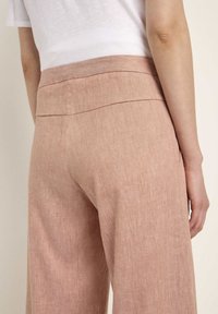 Light pink linen wide-leg pants with a smooth waistband, subtle texture, and clean seams, shown from the back with a partial view of the top.