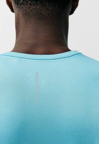 Camiseta deportiva azul claro hecha de material perforado, con escote redondo y detalle de costura vertical en la parte trasera.