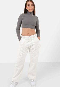 Grå ribbade kortärmade turtleneck med långa ärmar, tillsammans med vita vida byxor som har framfickor och en enda knappknäppning.