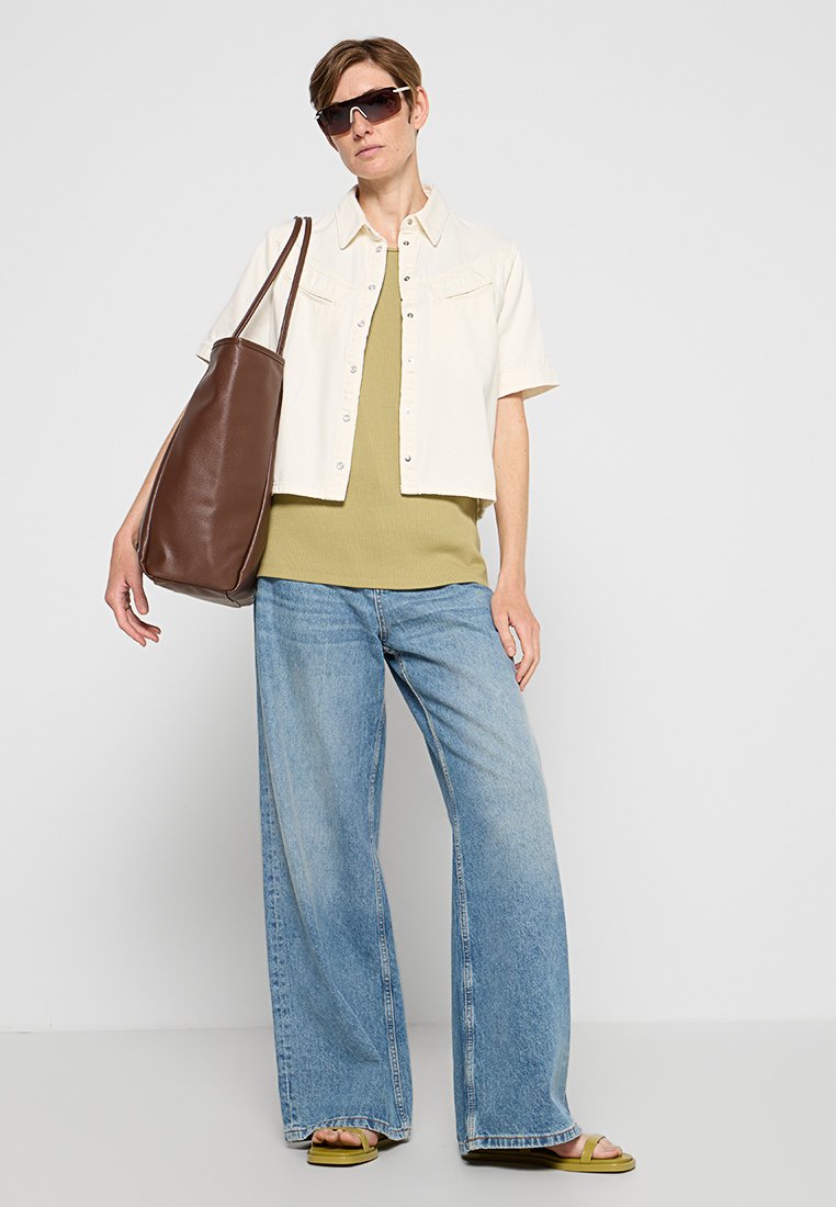 Licht beige korte mouwen jas, olijfgroene geribbelde top, wijde blauwe jeans, groene slippers en een bruine leren handtas. Zwarte zonnebril.