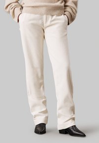 Lichtbeige corduroy broek met een relaxte pasvorm, voorzien van zijzakken en een textuurafwerking. Gepaard met zwarte puntige enkellaarsjes.