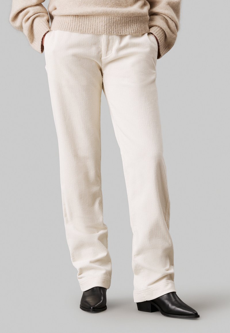 Lichtbeige corduroy broek met een relaxte pasvorm, voorzien van zijzakken en een textuurafwerking. Gepaard met zwarte puntige enkellaarsjes.