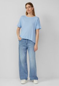 Lichtblauw, T-shirt met korte mouwen en een ronde hals. Gecombineerd met wijde, lichte spijkerbroeken en witte plateau sneakers.