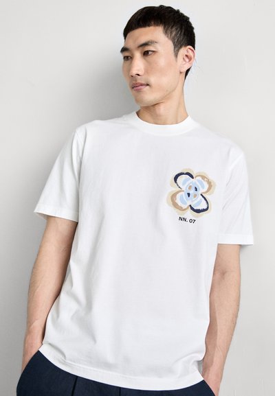 Hvid bomulds t-shirt med et frontprint af et flerfarvet abstrakt blomstermotiv. Korte ærmer og rund hals.