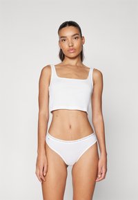 Top court blanc à encolure carrée et fines bretelles, associé à un string blanc avec une ceinture logotypée. Texture douce en coton.