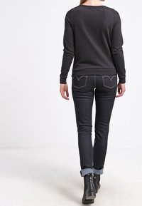 Svart långärmad topp med rundad halsringning, kombinerad med mörk denimjeans med uppvikt fåll och synlig sömnad på bakfickorna. Svarta ankelboots.