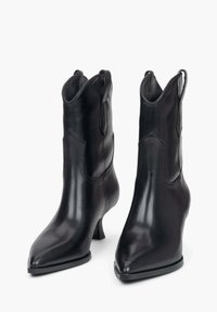 Czarne skórzane botki za kostkę z wąskimi przodami, niskim obcasem i dekoracyjnym przeszyciem. Posiadają boczne pętle do łatwego zakładania.