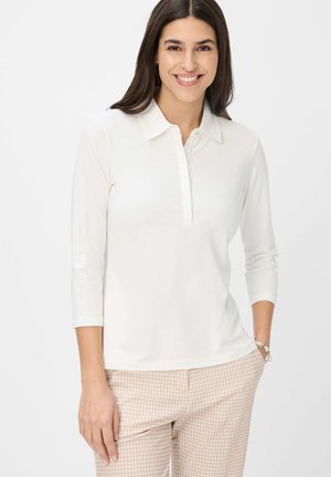 Weißes Langarm-Polohemd mit Kragen und Knopfleiste, kombiniert mit hellrosa Hahnentritt-Hose. Glatte Textur.