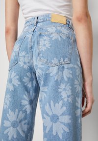 Lichtblauwe denim jeans met een madeliefjesprint, voorzien van een leren taillebandlabel, twee achterzakken en een rechte pijpdesign.