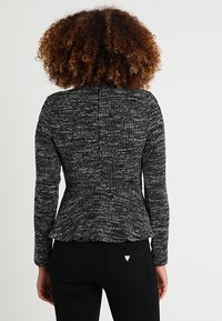 Giacca peplum texturizzata in bianco e nero con maniche lunghe, caratterizzata da una vita aderente e un orlo svasato, abbinata a pantaloni scuri.