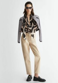 Blusa in seta nera e beige a fantasia, pantaloni in pelle beige, giacca cropped grigia texture, e mocassini neri con dettagli in oro.