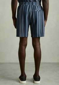 Marine-mønstret shorts med lodrette striber i et chevron-design. Elastisk talje med en baglomme. Bæret med sorte sneakers.