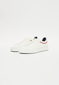 Sneakers bianchi in canvas con una finitura testurizzata, caratterizzati da accenti rossi e blu navy e lacci piatti. Punta rotonda e suola in gomma.