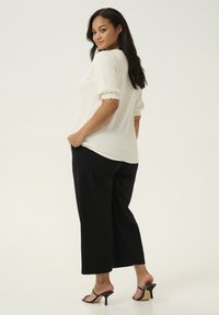 Weißes strukturiertes Oberteil mit drei Viertelärmeln, kombiniert mit schwarzen weiten Hosen und schwarzen Sandalen mit Absätzen. Minimalistisches Design und neutrale Farben.
