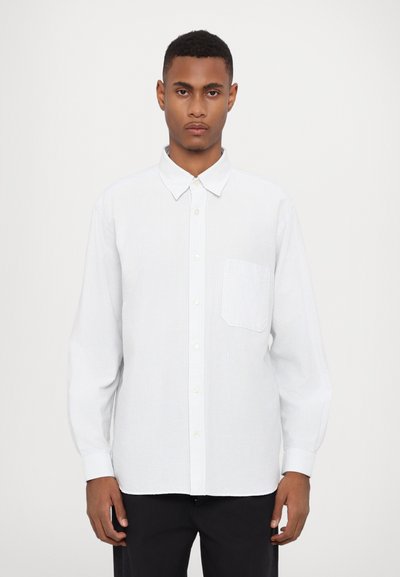 Camicia bianca con bottoni, decorata con una delicata fantasia a righe verticali, taschino sul petto e colletto classico; realizzata in tessuto leggero.