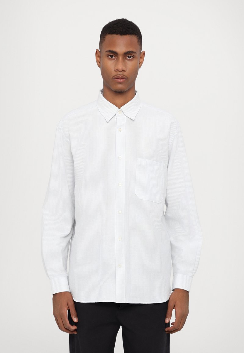 Camisa blanca de botones con un sutil patrón de rayas verticales, un bolsillo en el pecho y cuello clásico; hecha de una tela ligera.