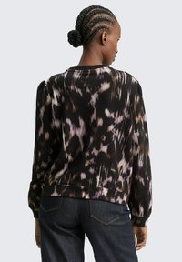Schwarzer Kapuzenpullover mit lila und braunem abstraktem Muster, mit Puffärmeln, gerippten Bündchen und Saum. Trägt man mit blauen Jeans, Rückansicht.