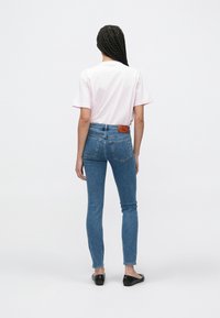 Ροζ μπλουζάκι, εφαρμοστά skinny τζιν από μπλε τζιν ύφασμα και μαύρα επίπεδα παπούτσια. Σημειώστε το δερμάτινο στοιχείο στη πίσω ζώνη με λογότυπο. Απλός και casual σχεδιασμός.