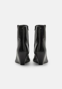 Bottines en cuir noir avec un talon compensé, présentant une texture lisse, des fermetures éclair latérales et un design minimaliste sans motifs visibles.