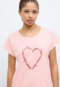 Ροζ βαμβακερό T-shirt με κοντά μανίκια, με κόκκινο κείμενο σε καλλιγραφικό στυλ που σχηματίζει καρδιά και λέει "amore" επανειλημμένα.