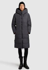 Lange grijze pufferjas met een hoge kraag, ritssluiting en elastische accenten. Heeft verticale stiksels, twee voorzakken en een ontspannen pasvorm.