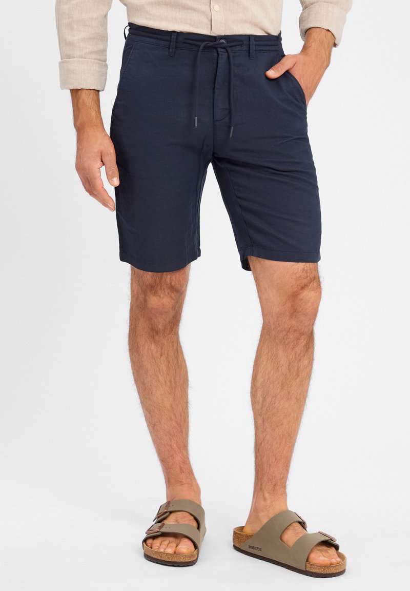 Marineblaue Leinen-Shorts mit einem elastischen Taillenbund und Kordelzug. Mit Seitentaschen und lässiger Passform, kombiniert mit braunen Schippersandalen.