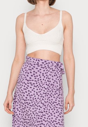 Witte geribbelde bralette met een V-hals ontwerp, gecombineerd met een lavendel wikkelrok met kleine donkerpaarse bloemenpatronen.