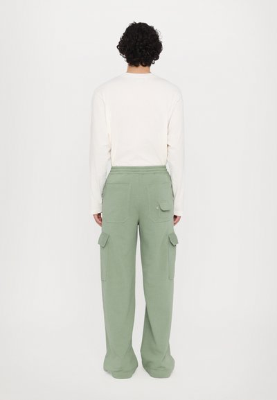 Green cargo pants with a relaxed fit, featuring side pockets and a drawstring waist, paired with a long-sleeve off-white top.