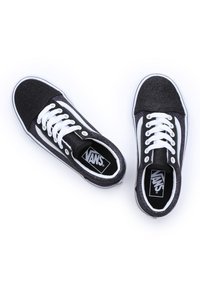 Zapatillas de deporte negras con purpurina, cordones blancos, franjas laterales blancas prominentes y un interior negro con el logo de Vans. Diseño clásico de caña baja.