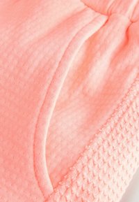 Tissu texturé rose clair avec une finition douce et lisse, doté d'une ceinture froncée et d'un détail de poche arrondi d'un côté.