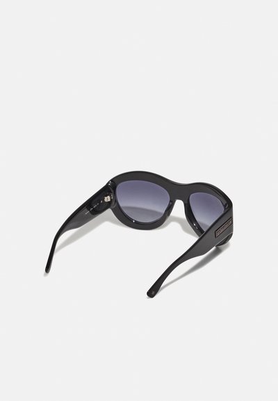 Lunettes de soleil noires avec des montures en plastique courbées, des verres dégradés foncés et des branches élégantes. Présente une marque sur le côté pour un détail supplémentaire.