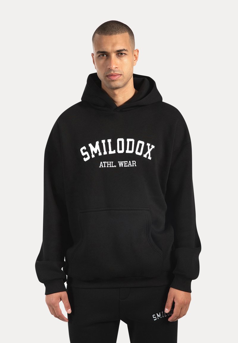 Sudadera negra hecha de material suave con un bolsillo frontal, que presenta el texto blanco "SMILODOX ATHL. WEAR" en el pecho y puños acanalados.