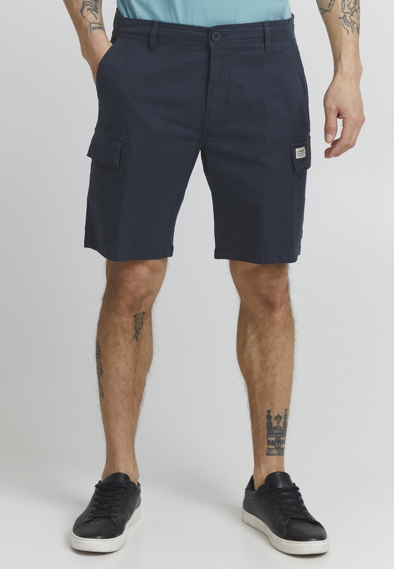 Mørkeblå cargo shorts laget av bomull, med front- og side lommer, knappelukking og en vevd etikett på siden. Teksturert stoff.