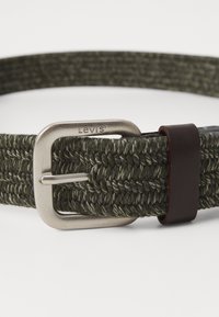 Flettet mørkegrøn stofbælte med en sølv metalspænde, mærket "Levi's", og en brun læderdetalje nær spænden.