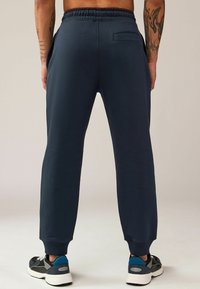 Pantalones de chándal marinos con cintura elástica, piernas ajustadas, bolsillos laterales y un bolsillo trasero, hechos de tela suave, combinados con zapatillas negras y azules.