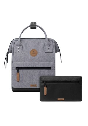 Grauer Stoff-Rucksack mit Frontreißverschlusstasche und schwarzer Leder-Setztasche, beide mit braunen Markenlabels und Zugschnüren.