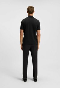 Black polo shirt paired with black trousers. The shirt features a collar and short sleeves, with a smooth, even texture.
