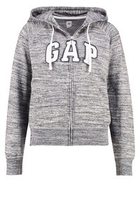 Felpa grigia con zip realizzata in tessuto testurizzato, dotata di cappuccio regolabile, tasche frontali e audace logo "GAP" sulla parte anteriore.