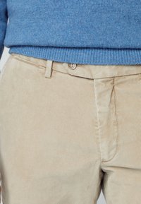 Beiga manchesterbyxor med texturerade vertikala ränder, med knäppning och en blå stickad tröja ovanför.