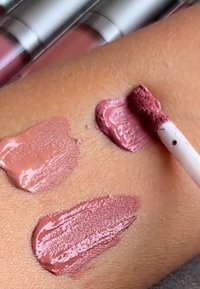 Kolme vaaleanpunaisen nestemäisen huulipunan sävyä testattuna iholla, yksi sävy levitetty applikaattorilla.